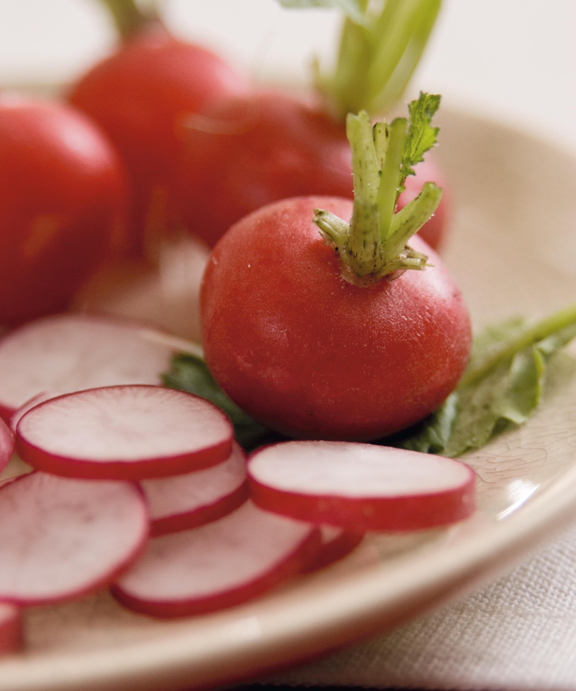 Whole red round radishes on a plate alongside slices of radishes with white flesh