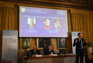 A member of the Nobel Committee for Physics speaks to the media in front of a screen showing the portraits of the laureates of the 2019 Nobel Prize in Physics: (left to right) James Peebles, Michel Mayor and Didier Queloz, during the announcement of the winners of the 2019 Nobel Prize in Physics at the Royal Swedish Academy of Sciences on Oct. 8, 2019.