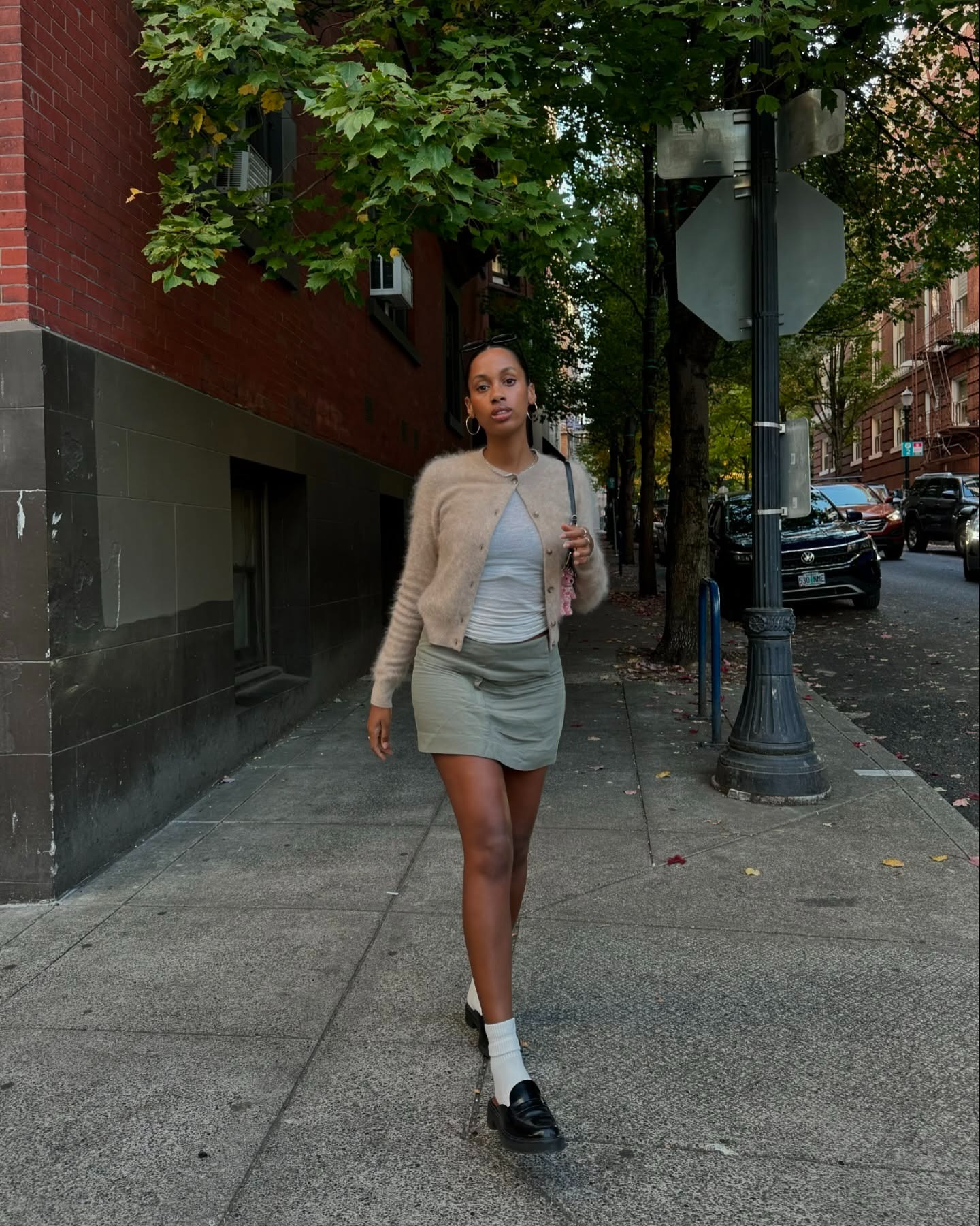 Claire Most wearing a cardigan, green mini skirt, socks, and patent-leather loafers.