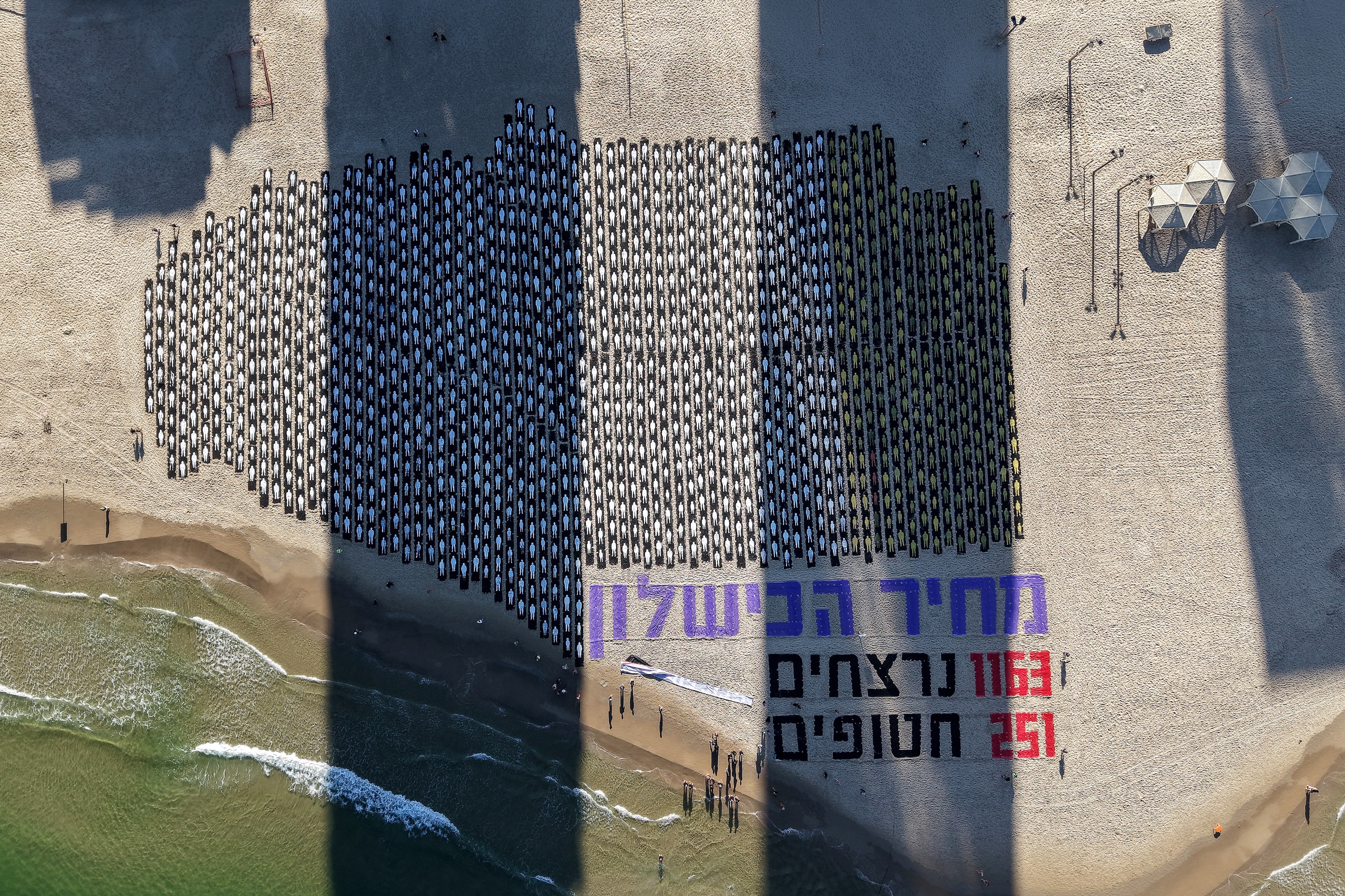 An aerial view shows people standing on the beach next to a commemorative installation marking the third anniversary of Hamas's October 7 attack on Israel, in Tel Aviv on October 7, 2026.