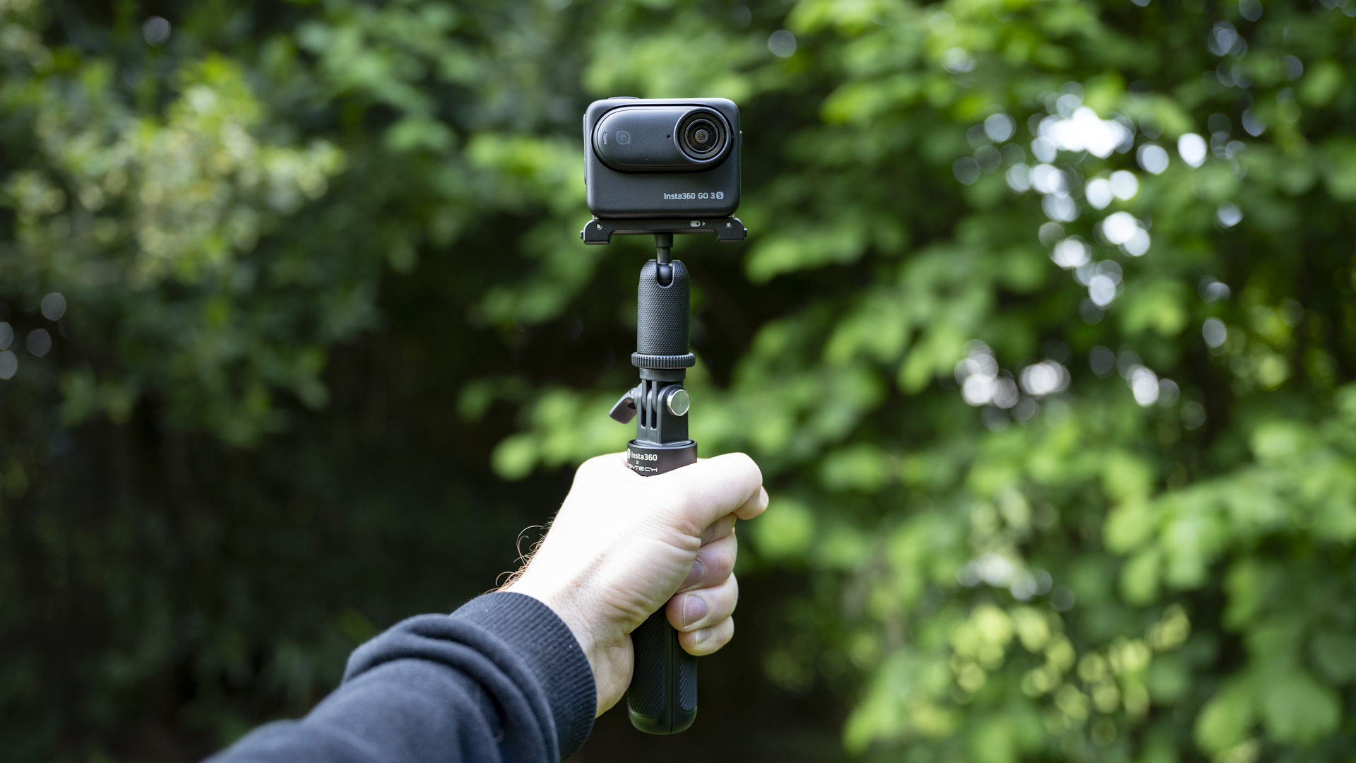 Insta360 Go 3S camera in its housing attached to a selfie stick, outdoors