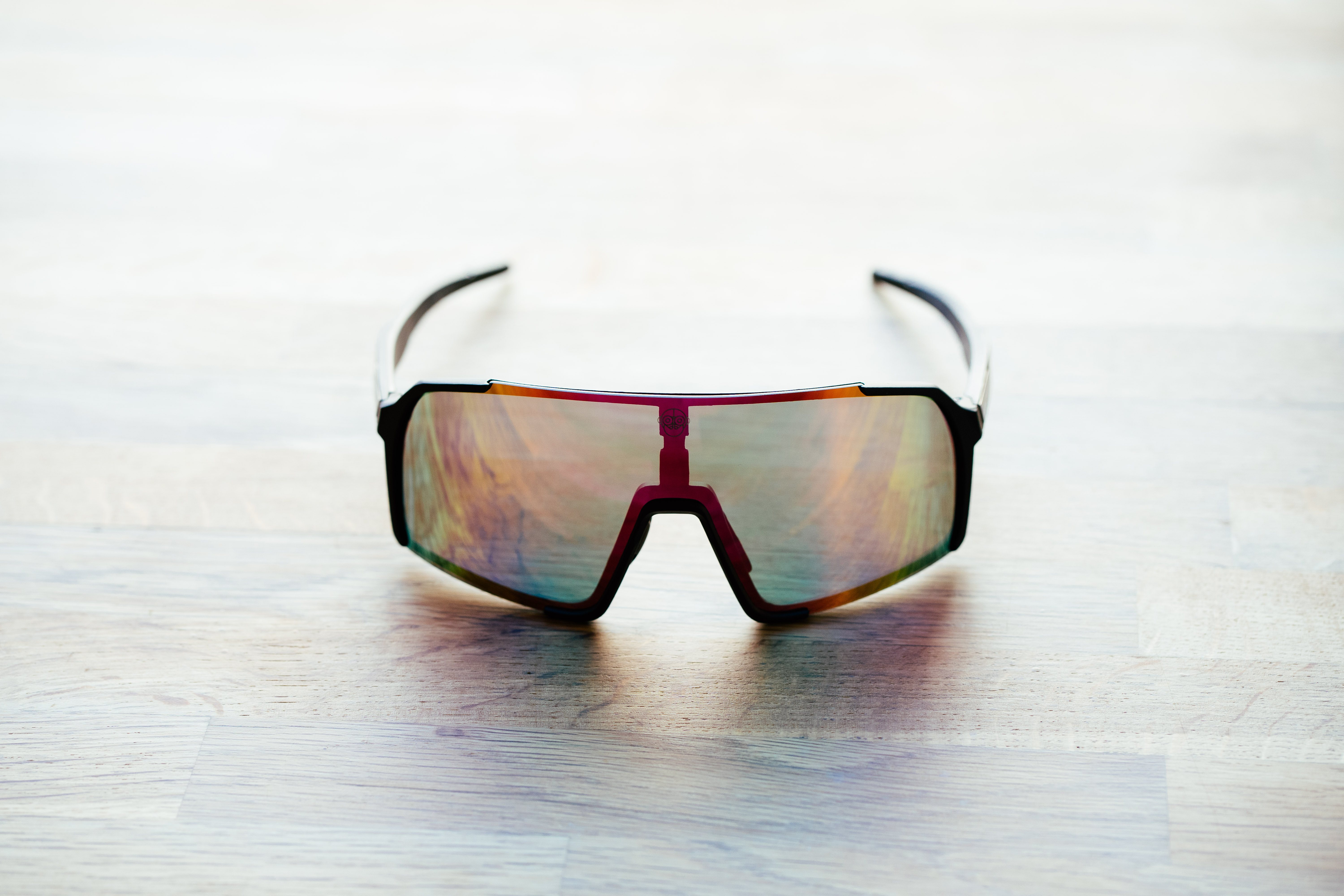 A set of black frame sunglasses with irridescent lenses on a wooden surface