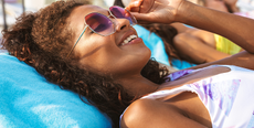 A woman laying on a sun lounger wearing sunglasses and a swimsuit from Bare Necessities.