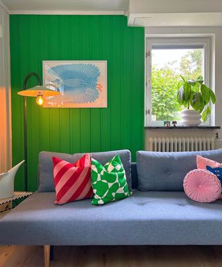 A green small living room with a gray couch with colorful pillows