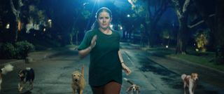 amy adams runs in the street with several dogs in a still from nightbitch