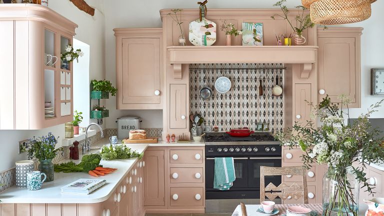 kitchen with pink cabinets and pink and grey geometric tiles above range cooker rattan lampshades and flowers on table
