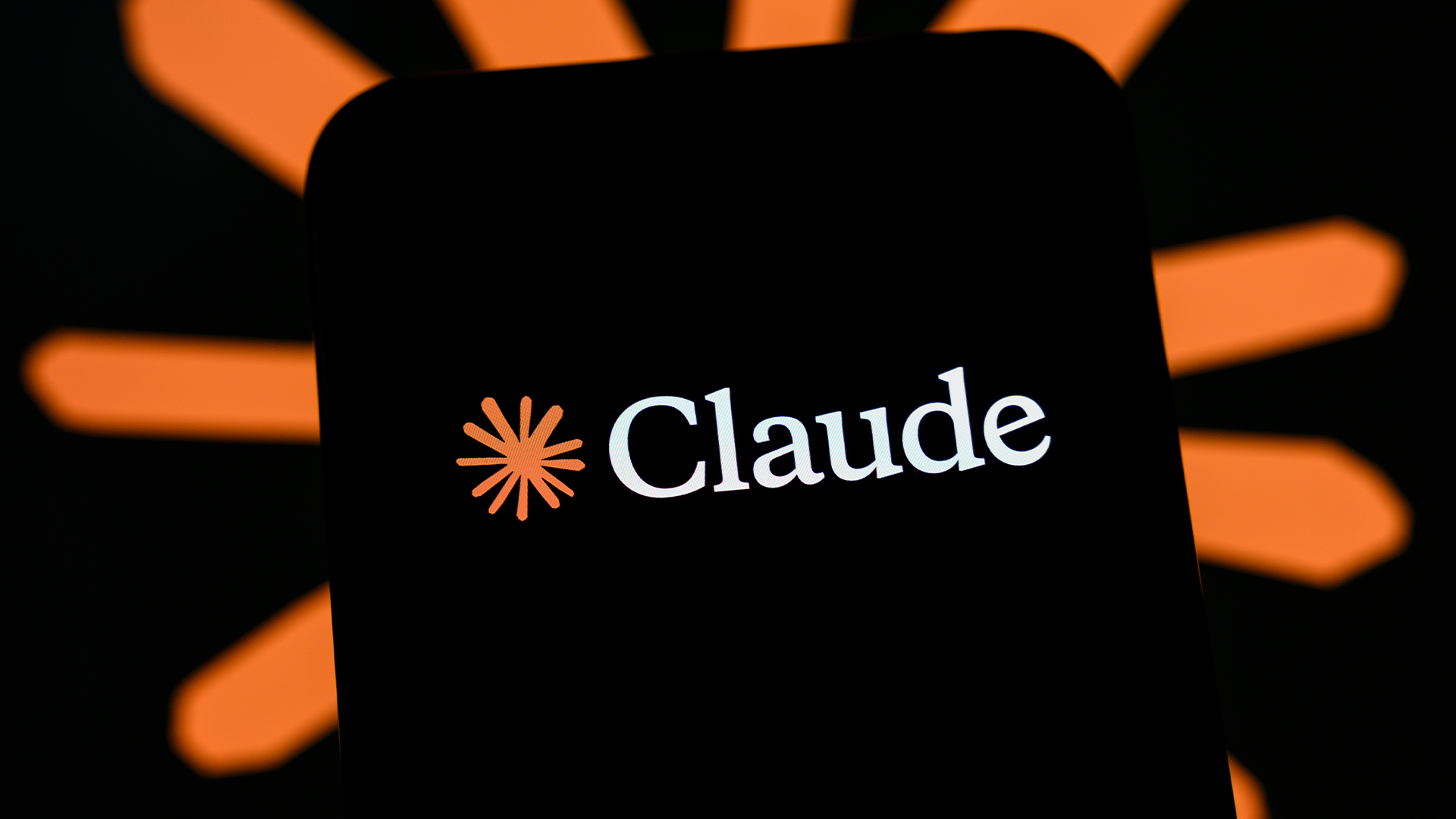 Anthropic Claude AI logo pictured on a smartphone screen, with AI tool branding blurred in background.