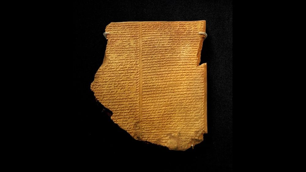 An ancient clay tablet with inscriptions engraved on it photographed against a black background. 