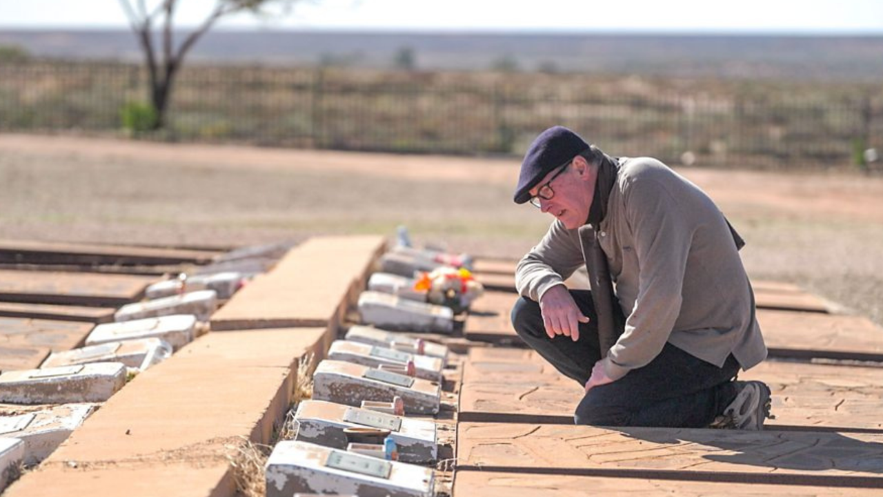 Journalist Colin James kneels by graves in the Woomera cemetery in Maralinga, Australia 