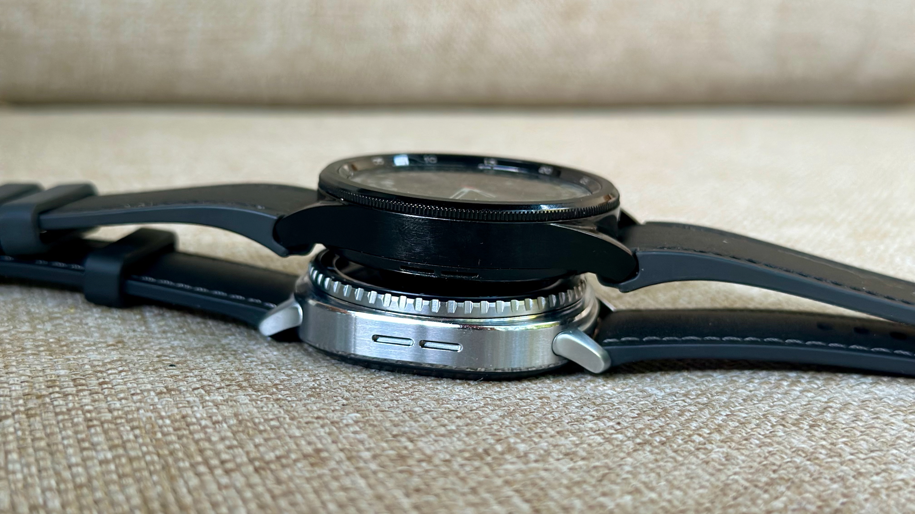 The Samsung Galaxy Watch 6 Classic (top) sitting on top of the Samsung Galaxy Watch 6 Classic (bottom), the photo angled to show their thickness and the difference between the curved 6 case and flat 8 case. 