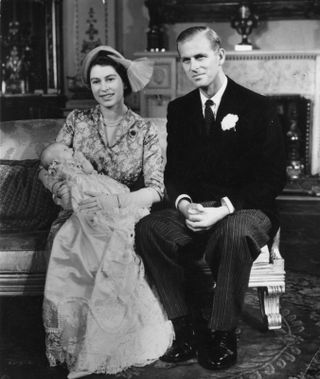 Princess Elizabeth (later Queen Elizabeth II) holding her daughter Princess Anne at her christening with the Duke of Edinburgh at her side.