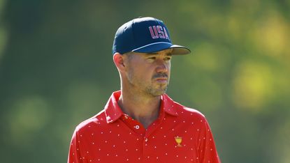 Brian Harman looks on at the Presidents Cup while wearing a navy blue USA cap and red polo