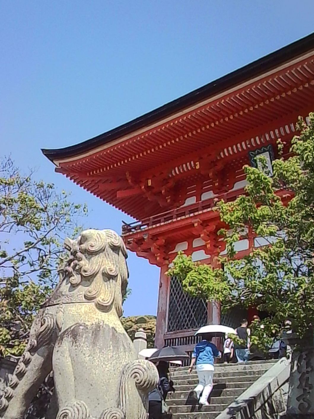 Stone guardian statue beside the steps of a red Japanese temple building.