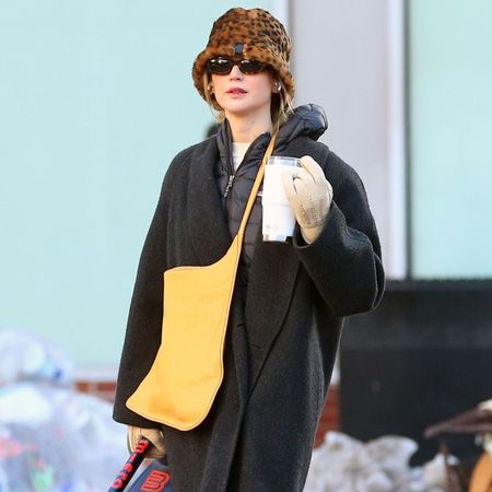 Jennifer Lawrence walks down the street wearing a black coat with Uggs, red trousers and a leopard print hat.