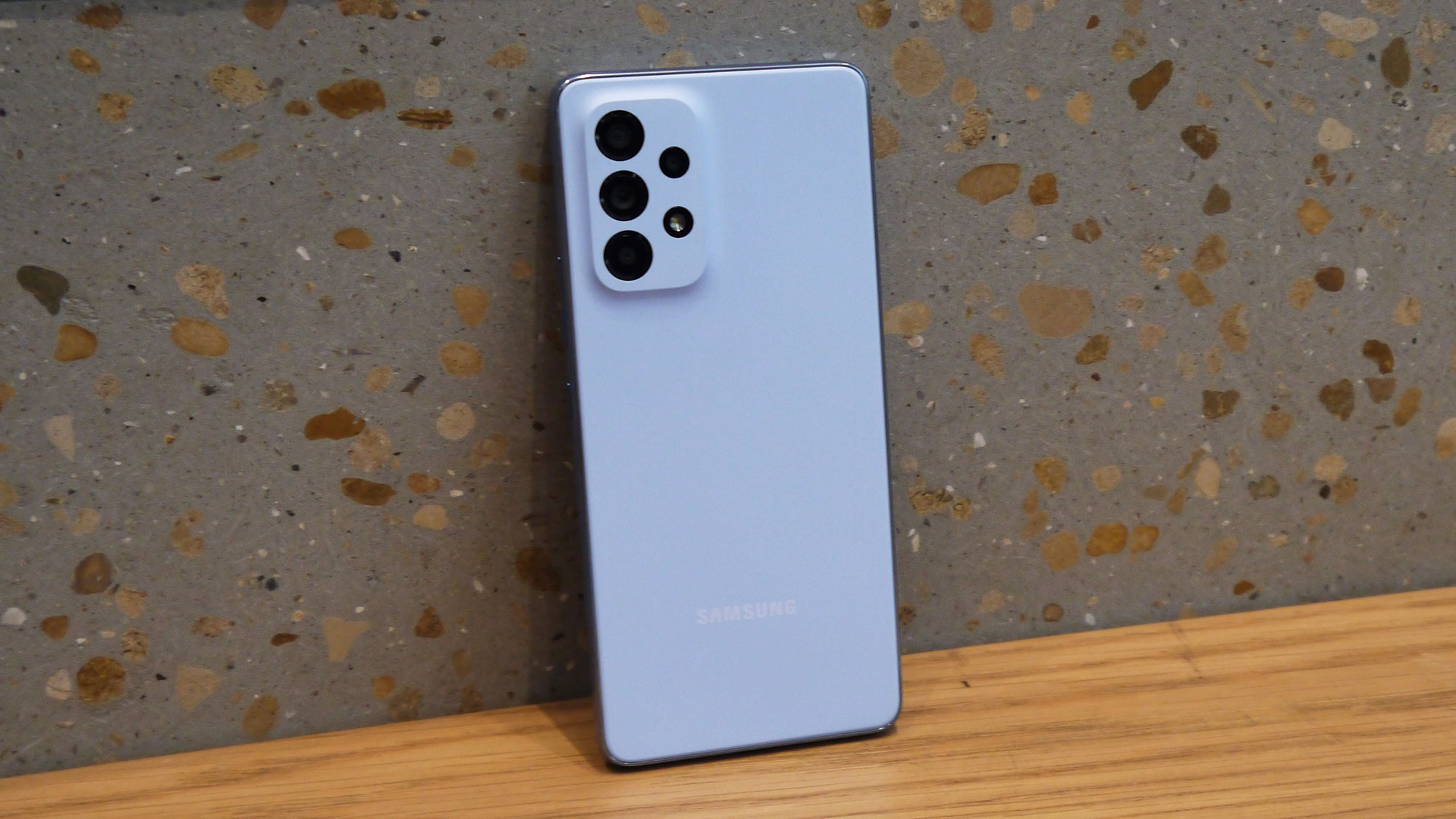View of the rear of the Samsung Galaxy A53 5G standing upright against a concrete wall