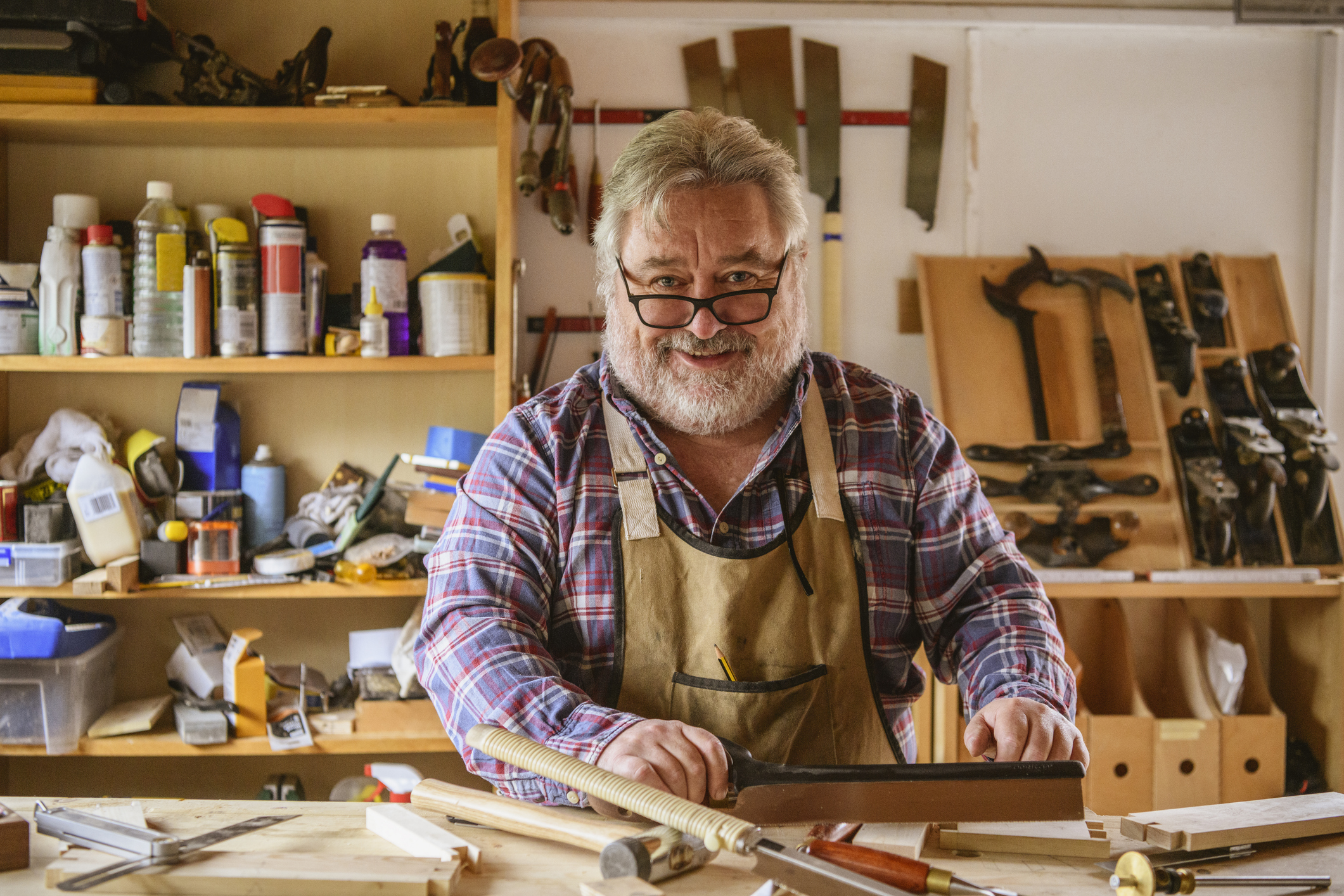 A retired man smiles in his carpentry shop, surrounded by tools and supplies.