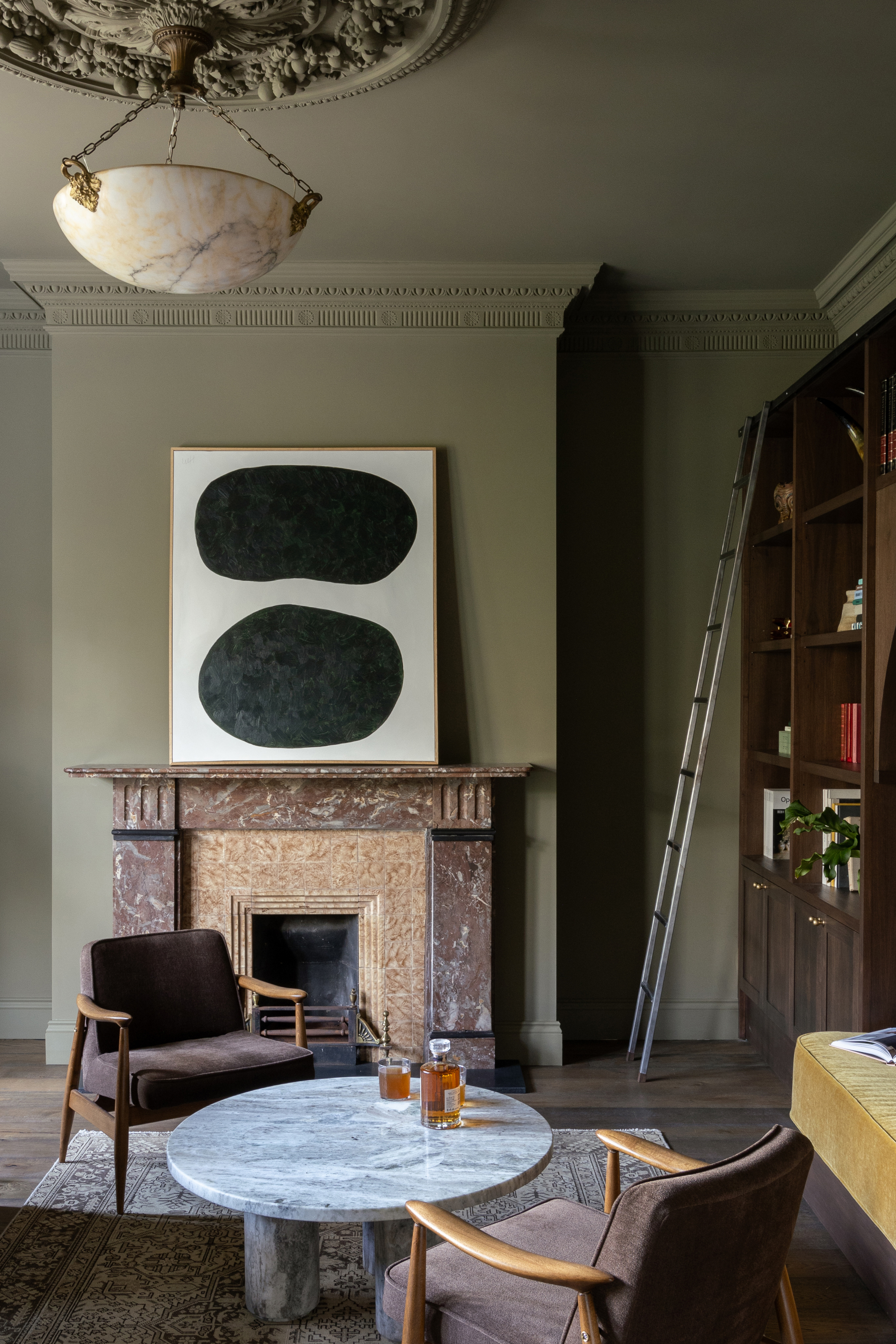Deep green living room with brown stone fireplace, brown armchairs and grey coffee table, with black and white abstract artwork on mantlepiece