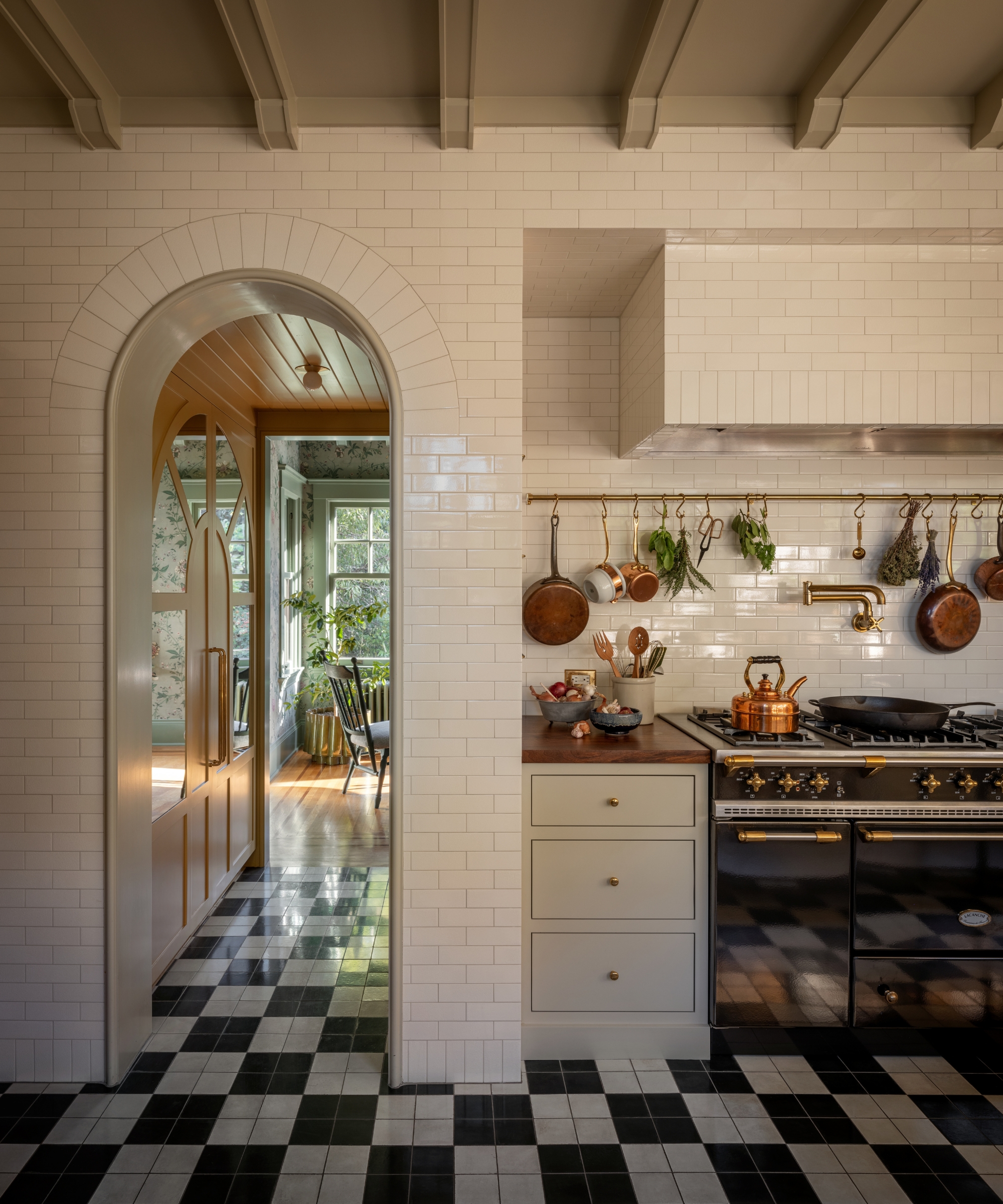 a small white kitchen with tiles walls and a black range cooker with a brass pot rack on the wall above