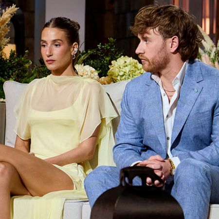 amanda batula wearing a yellow dress and west wilson wearing a blue suit looking tense while appearing on the summer house season 10 reunion