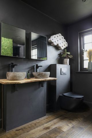 Black bathroom with wooden floor panelling, twin sinks, black taps and twin mirrors