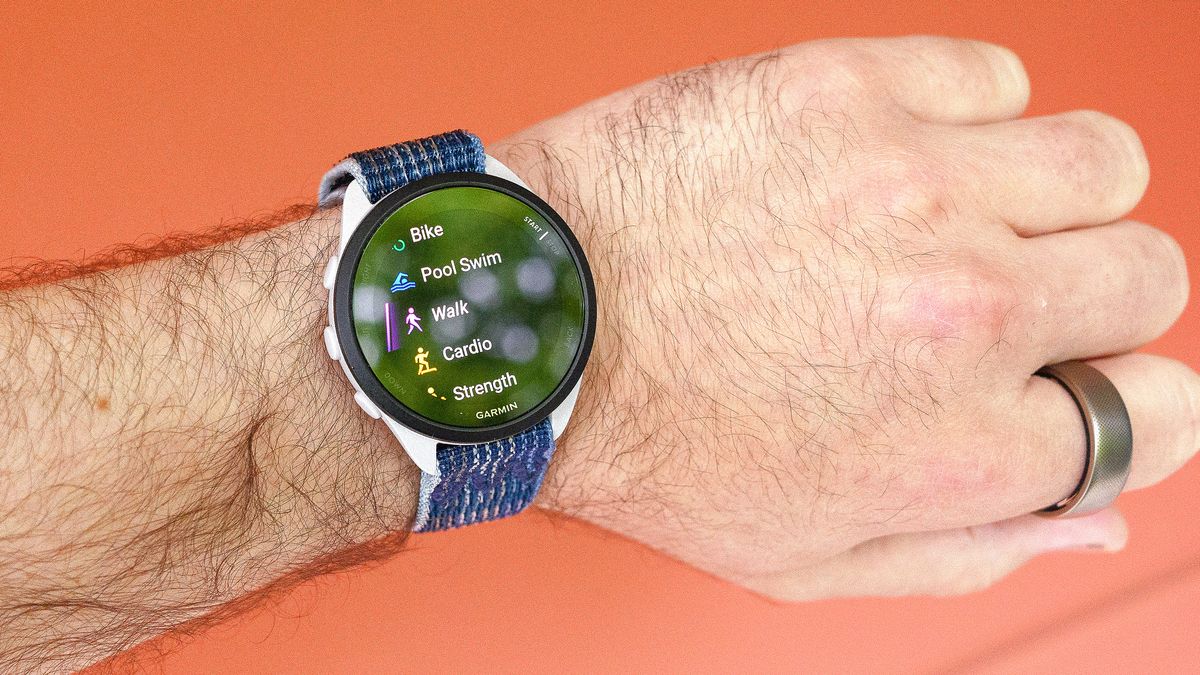 Helio RIng and Garmin Forerunnr 165 smartwatch on a user&#039;s wrist against an orange background.