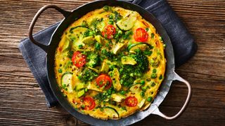 Skillet holding vegetable omelette sitting on cloth on rough wooden table