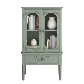 A green accent cabinet with glass doors and books and vases within it