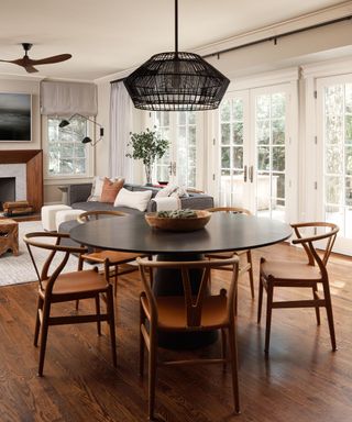 An open-plan living and dining room with glass paneled doors, a black dining table, and a wooden-paneled fireplace