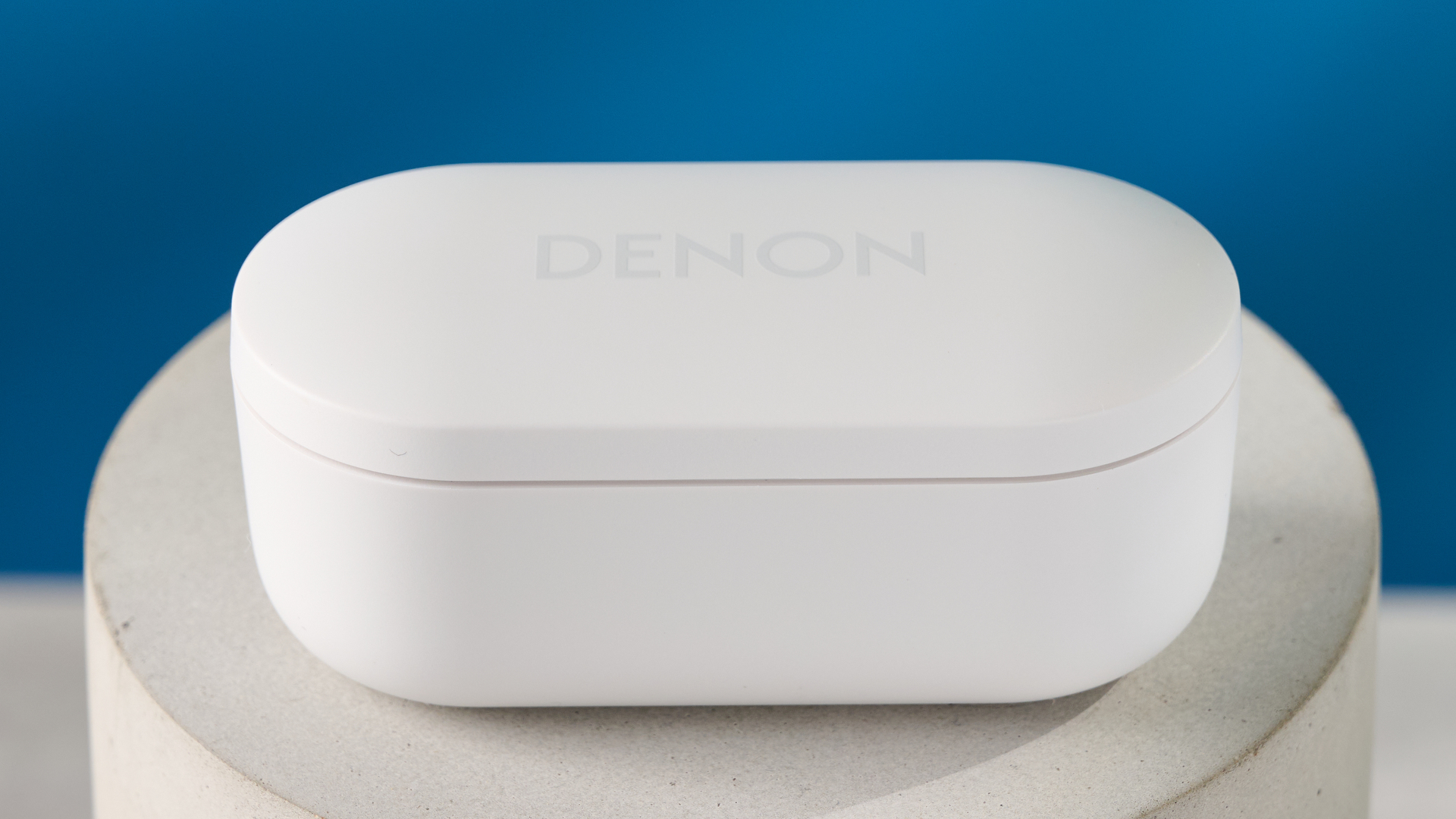 the denon perL Pro wireless earbuds in white, with circular earbud shapes, and a white charging case, photographed against a blue background