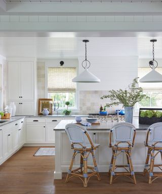 white kitchen with wood flooring and woven light blue bar stools and pair of pendant lights