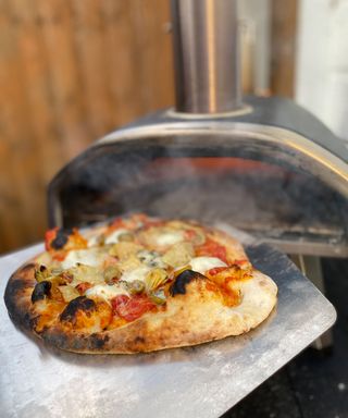 taking a cooked pizza out of an outdoor oven