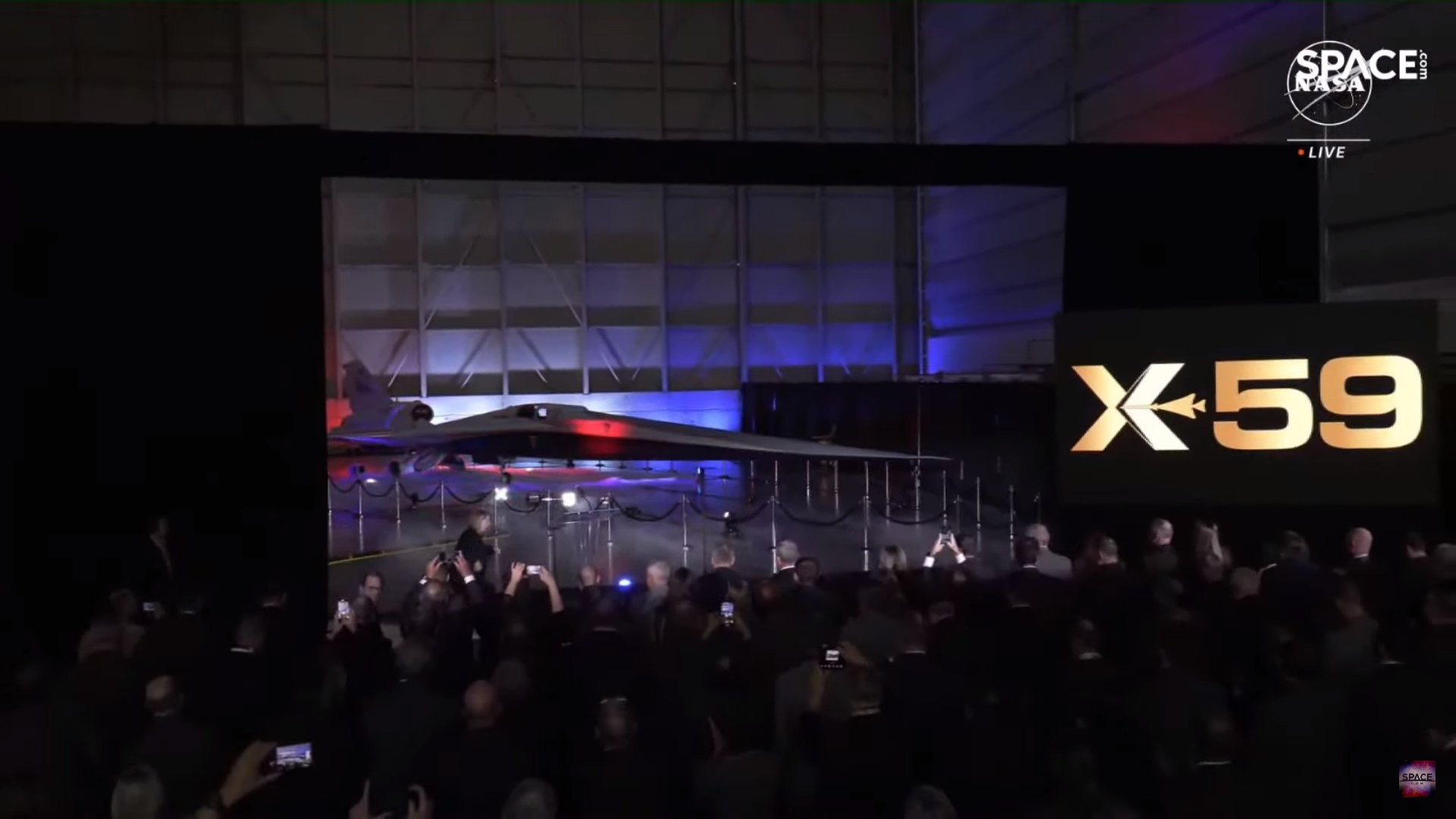 A crowd watches a sleek supersnic jet revealed in a hangar