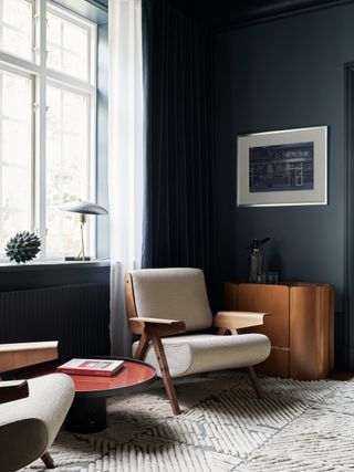 two armchairs positioned in the corner of living room near a window with a side table, lamp, artwork on the wall