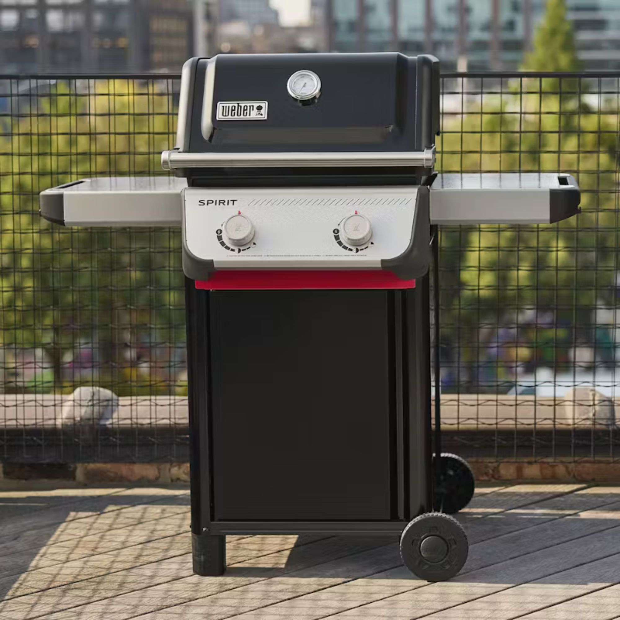 Weber Spirit E-210 Gas Grill on concrete against a fence. 