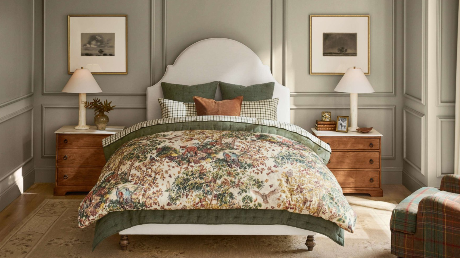 a bedroom with a forest-themed bedspread, sage green painted walls, symmetrical bedside tables and lamps, and a plaid accent chair
