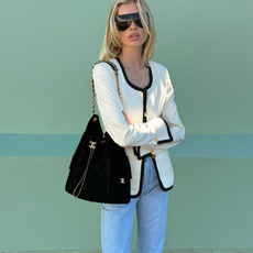 Photo of Elsa Hosk wearing white jacket with black trim, black Chanel bag, and light wash jeans.