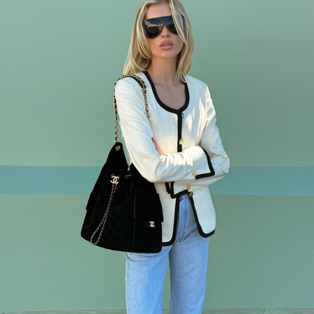 Photo of Elsa Hosk wearing white jacket with black trim, black Chanel bag, and light wash jeans.