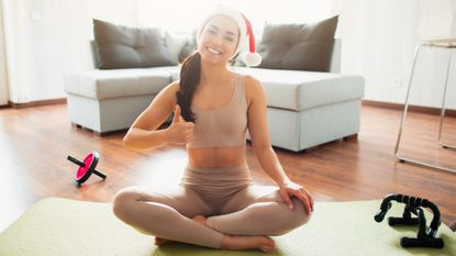 Person showing thunmb up sitting on an exercise mat wearing a Christmas hat