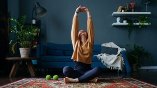 Woman reaching arms above her head stretching on living room floor, doing yoga workout at home