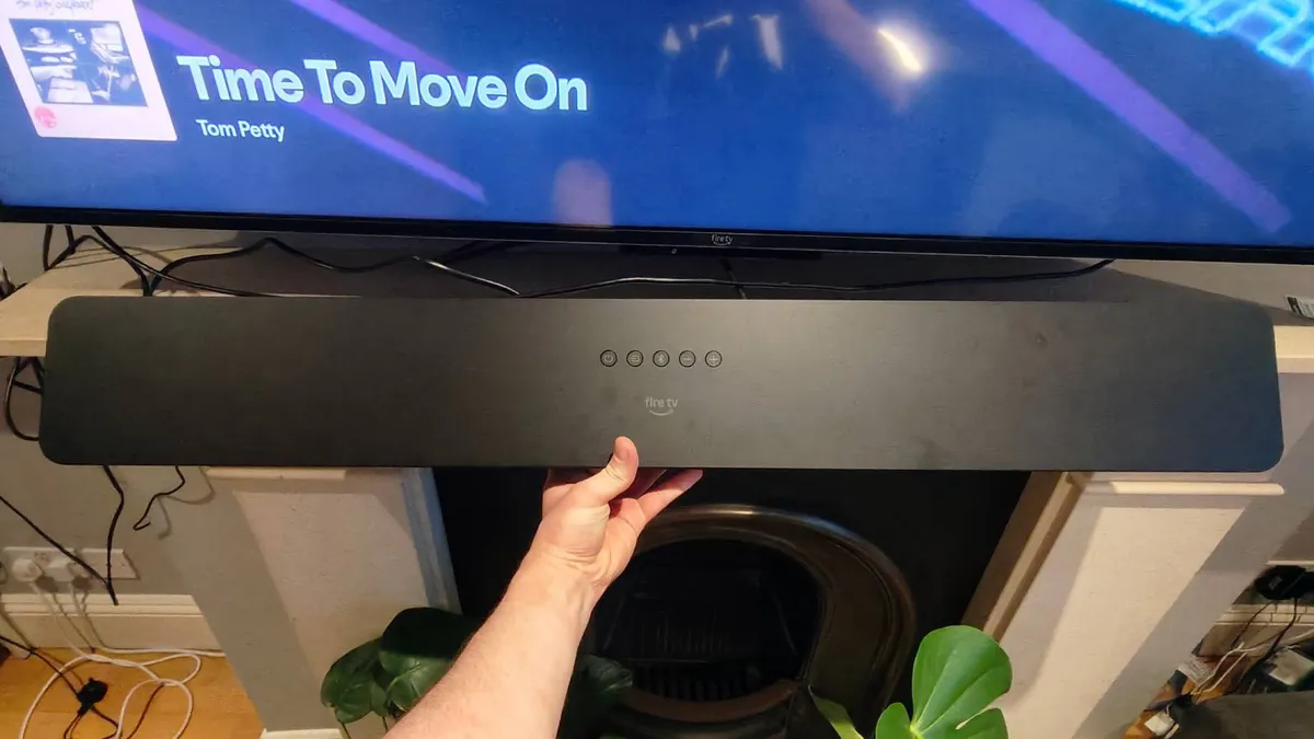 The Amazon Fire TV Soundbar Plus being held in front of a TV showing Spotify.