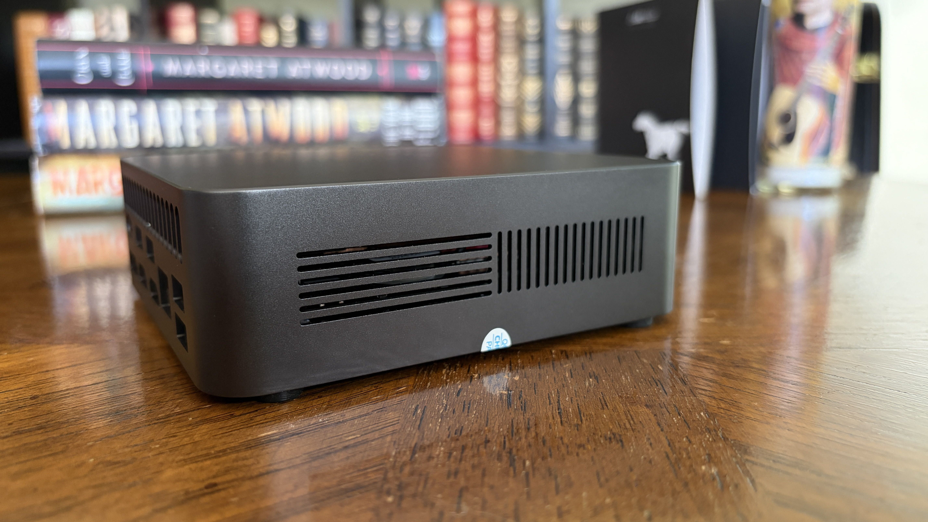 Small black Chuwi mini PC with ventilation slits on a wooden table, books in the background.