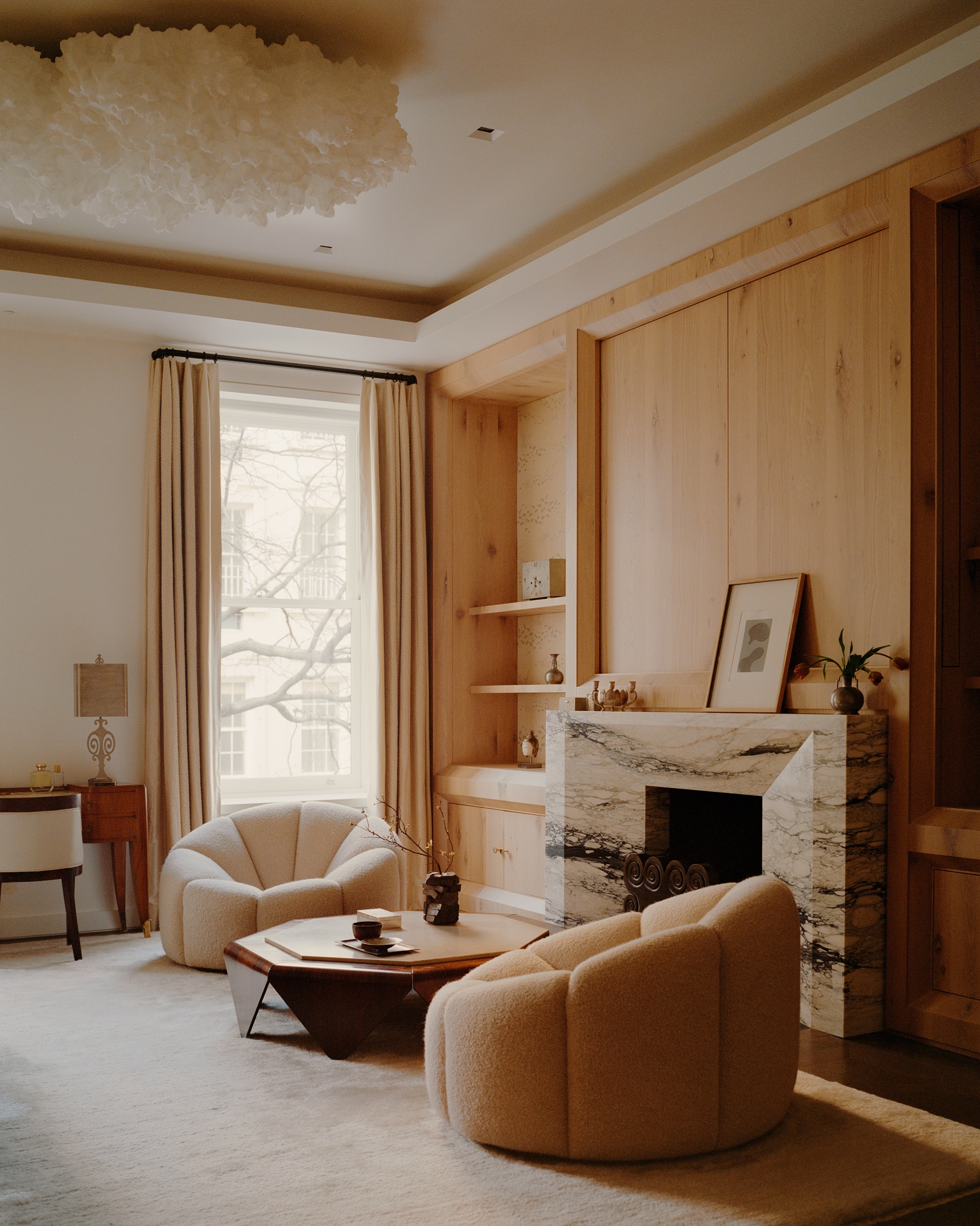 a bedroom sitting area with a wooden paneled wall, marble fireplace and comfortable seating