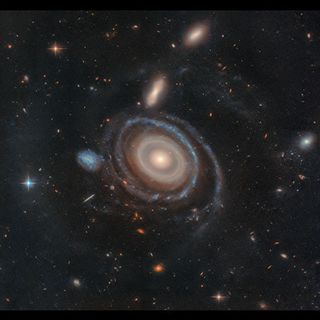 A swirling galaxy like a bullseye with blue and tan and orange gases around a central bright point.