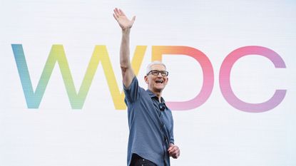 Apple CEO Tim Cook at WWDC 25, waving to the crowd with the "WWDC" logo behind him
