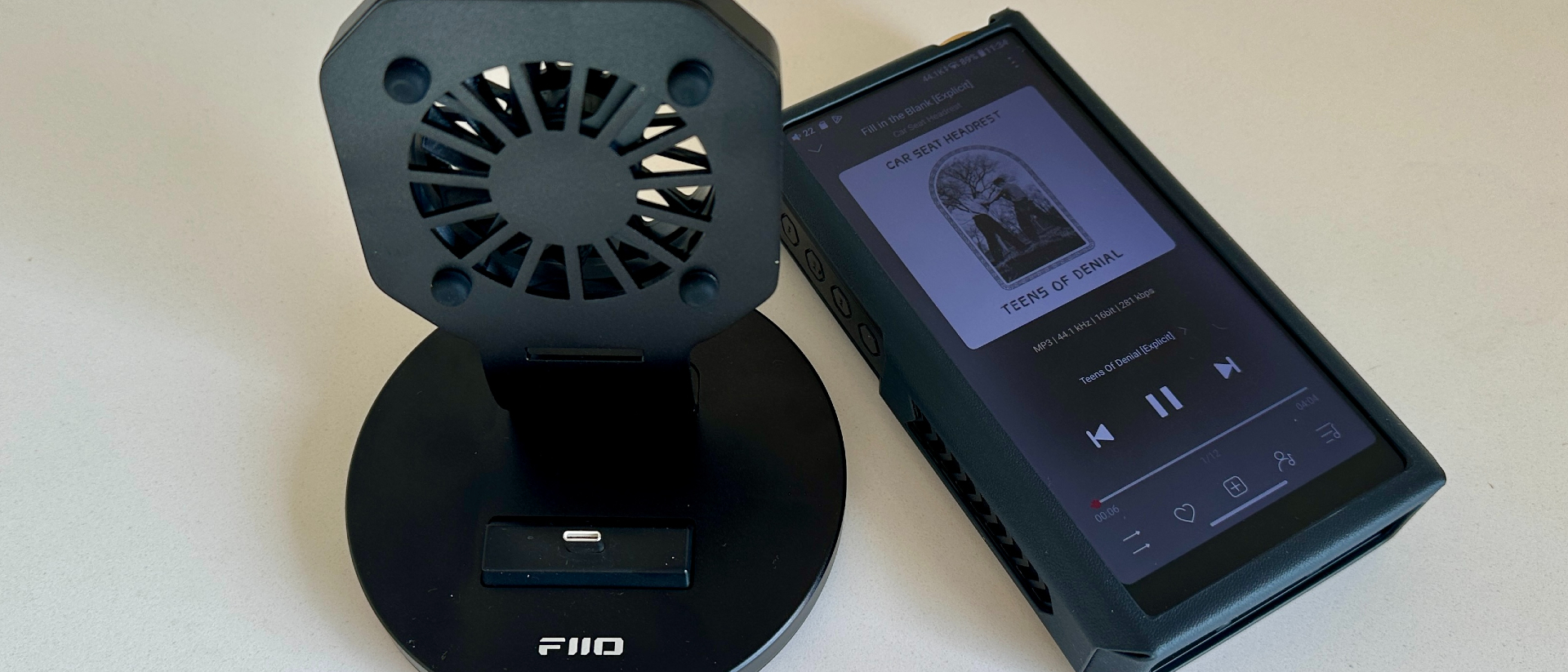 The FiiO M27 player with screen and dial showing, and content on the screen, on beige or yellow background