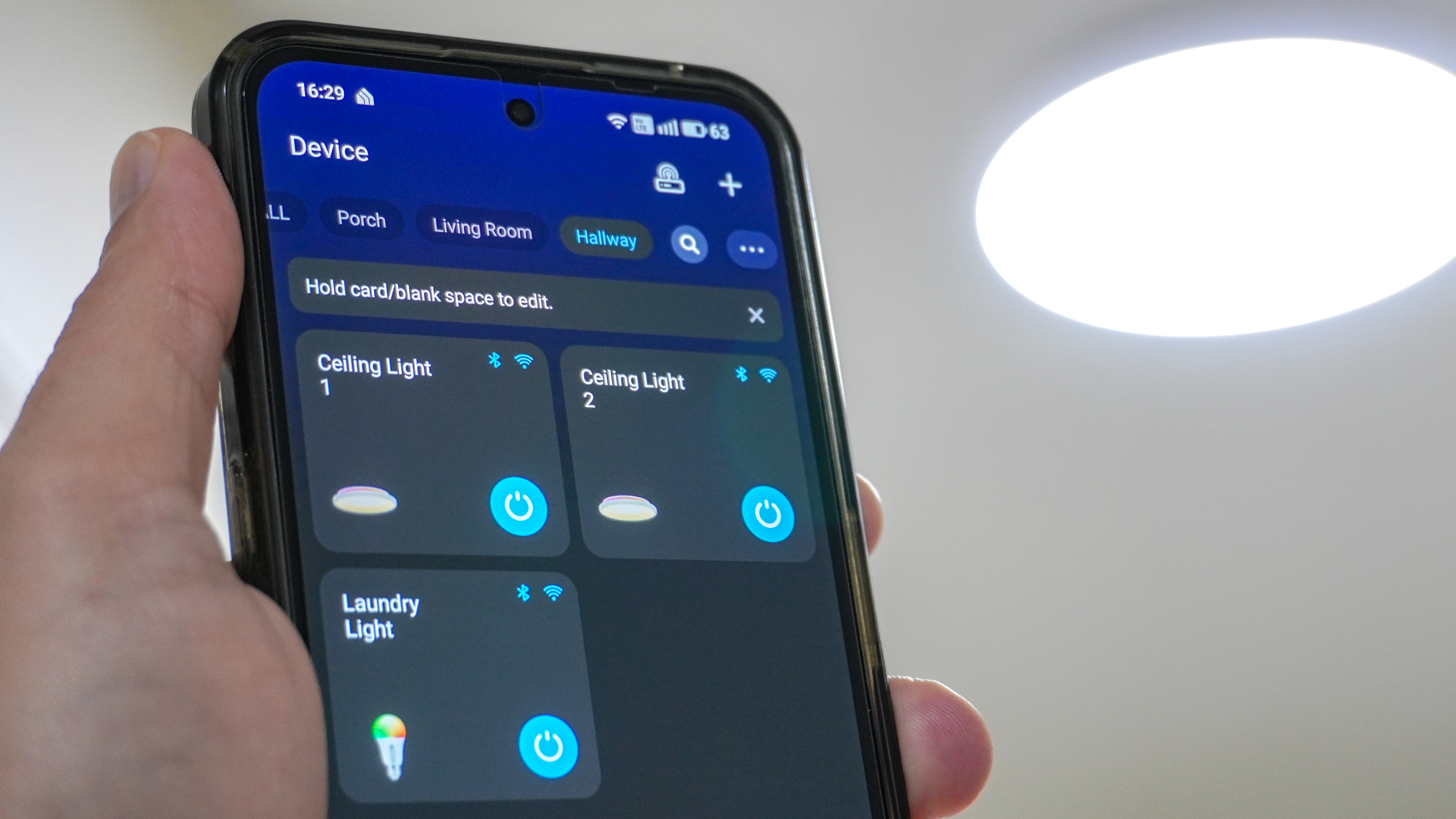 A person holding a phone with the Govee app open showing its home screen with a Govee smart light in the background