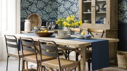 Dining room with blue patterned wallpaper, modern country wooden furniture and a rattan pendant over the table