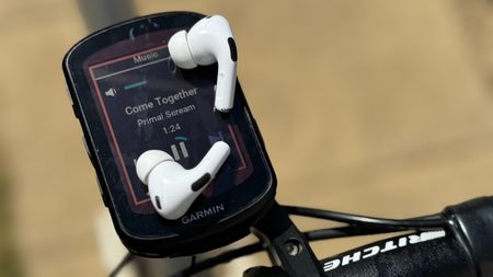 Apple AirPods resting on a Garmin bike computer screen showing Primal Scream playing