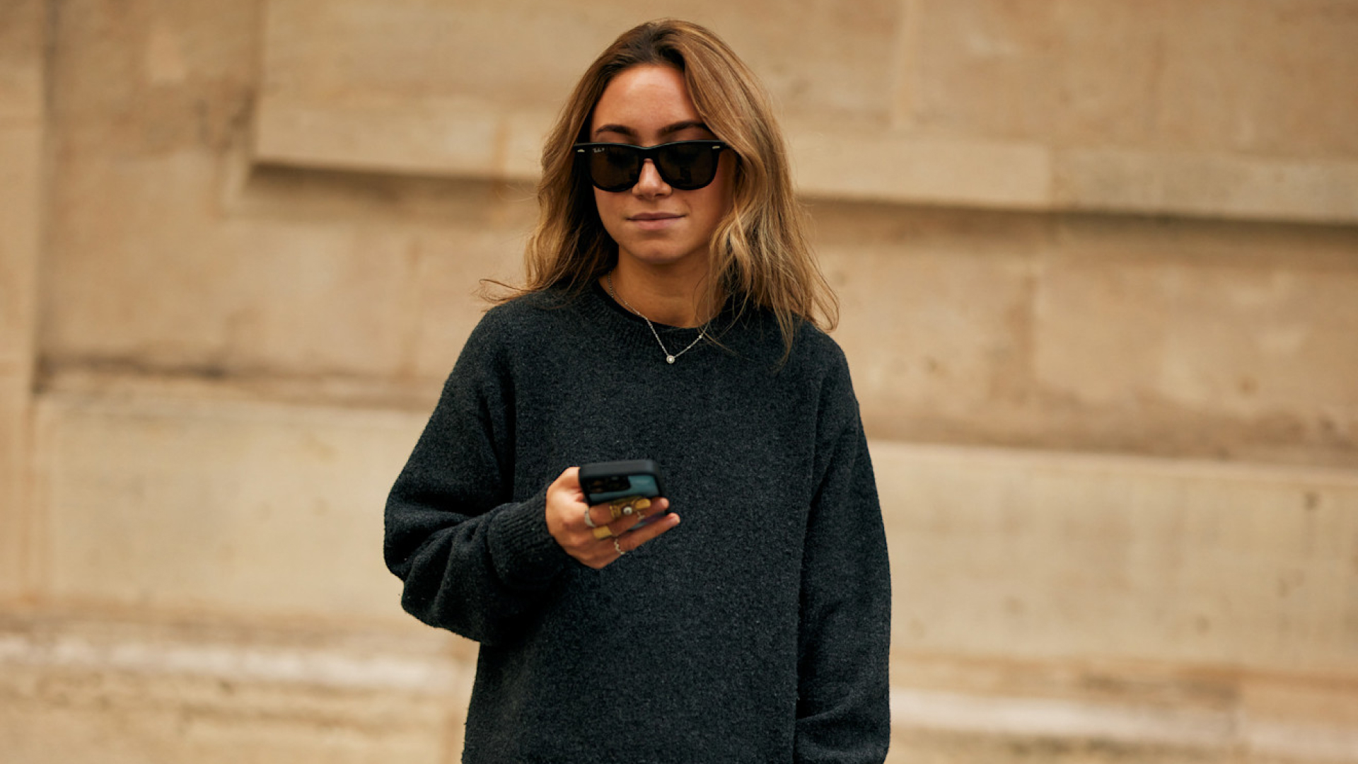 fashion week attendee wearing sunglasses and grey sweater holding phone