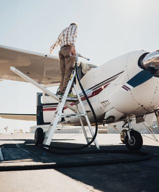 A man in a flannel putting fuel into his small Cessna plane.